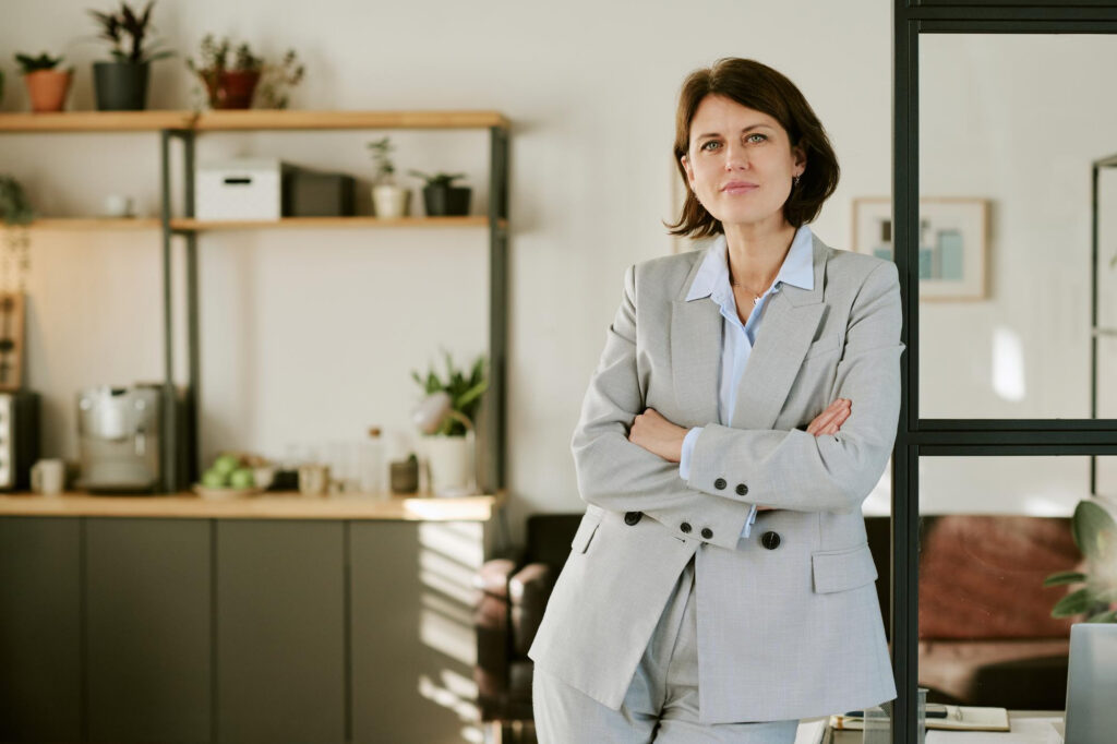A woman in a grey suit standing with arms crossed in an office setting
