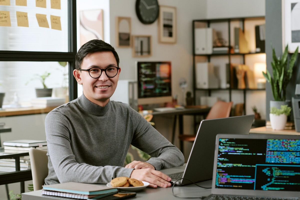 A man smiling at a desk with a laptop displaying code