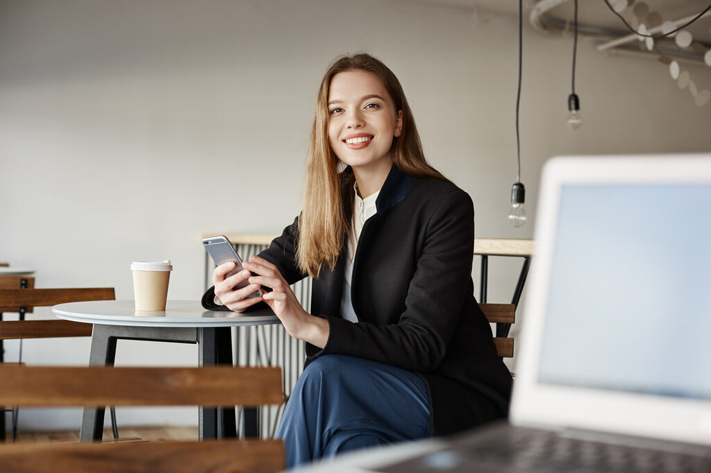 A woman smiling while sitting at a table with a laptop.