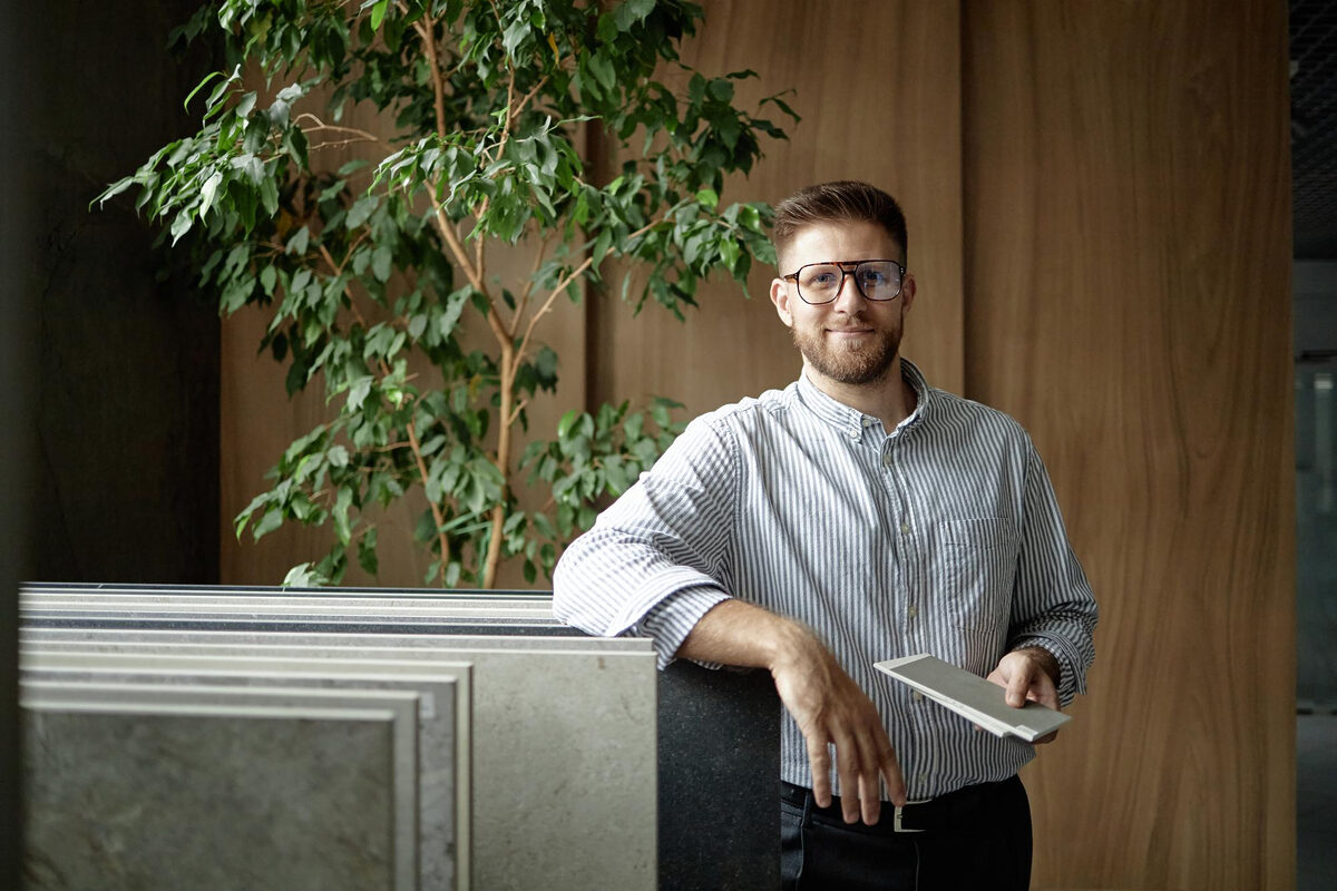 A man leaning against a desk in a stylish office, holding a notepad