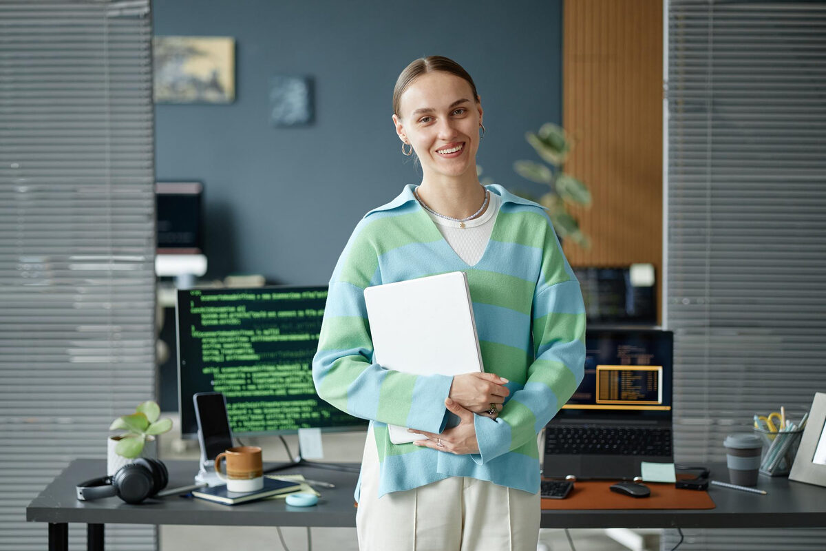 A woman standing in an office next to a desk with data codes on computer.