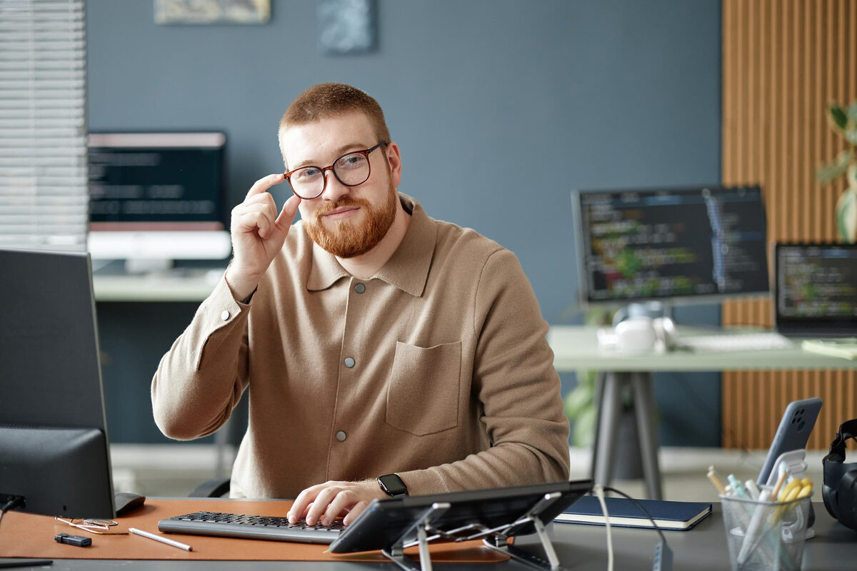 A man with glasses working at a dual-monitor office desk.