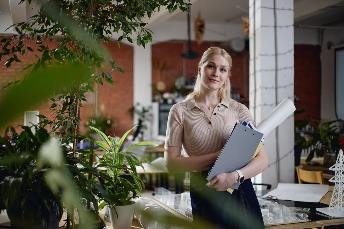 A woman standing in a office among plants, holding a folder