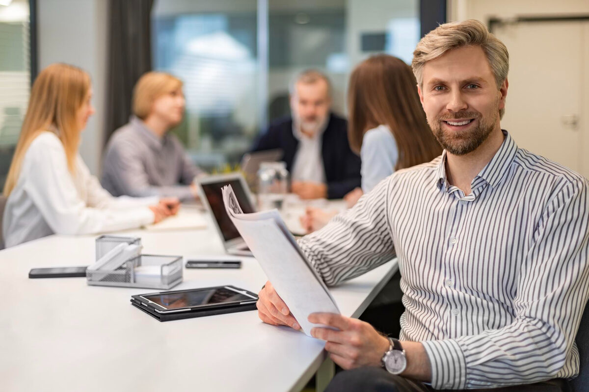 A man sitting in a meeting room holding a report with his team discussing