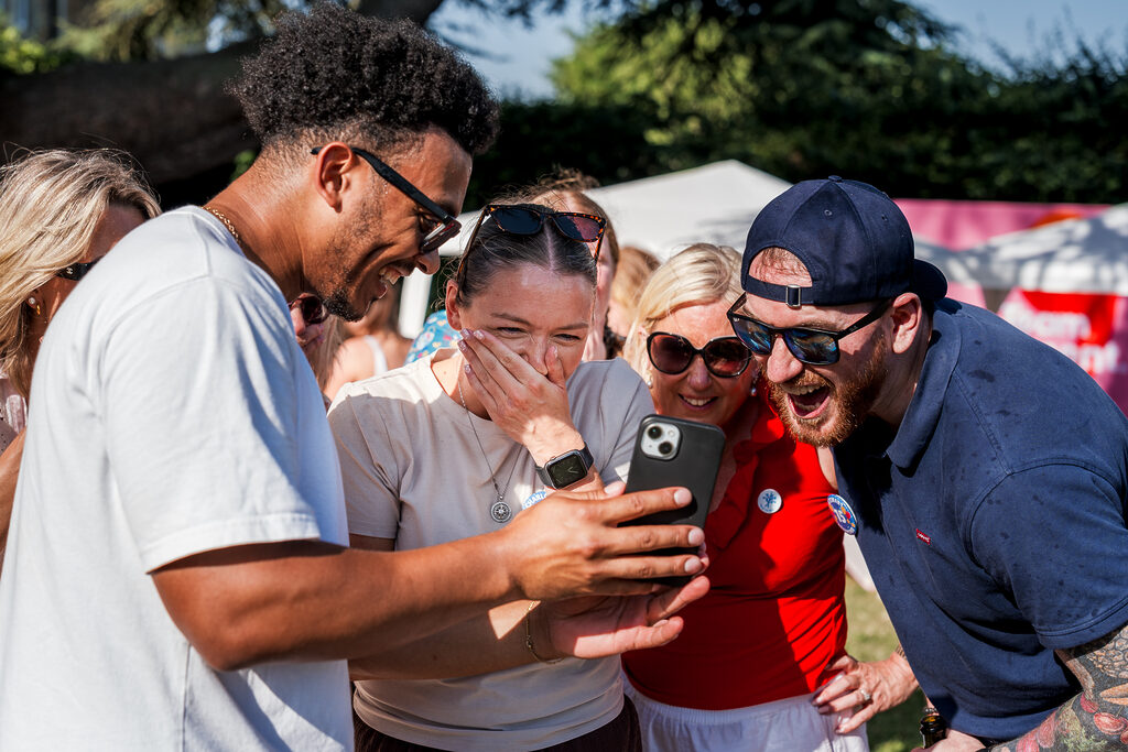 Group of colleagues laughing together while looking at a phone outdoors